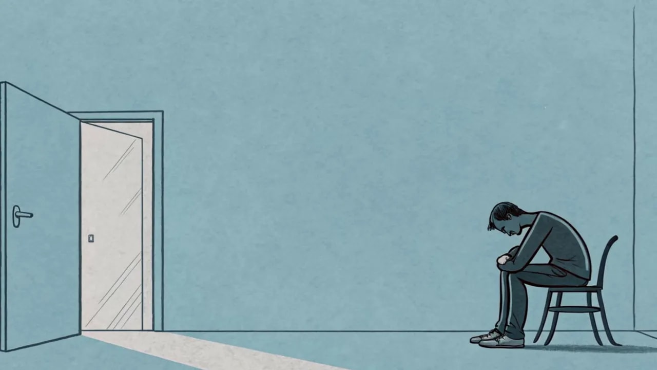 Person sitzt zusammengesunken auf einem Stuhl in einem leeren Raum; eine offene Tür lässt Licht herein